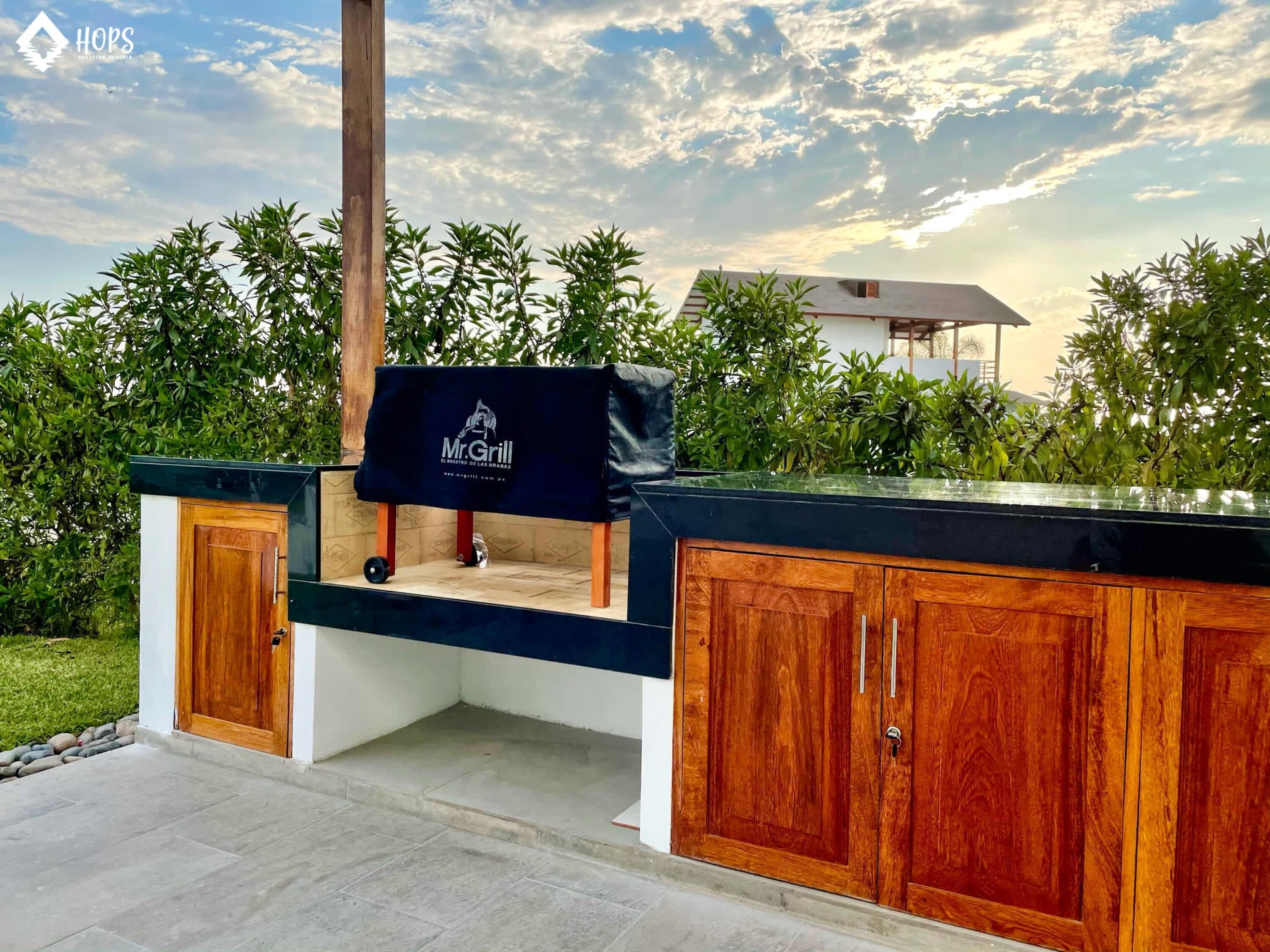 Un'area cucina all'aperto con angolo barbecue, pensili in legno e vista sul cielo.