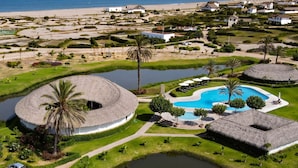 Um resort com piscina circular, piscina retangular e área de praia.