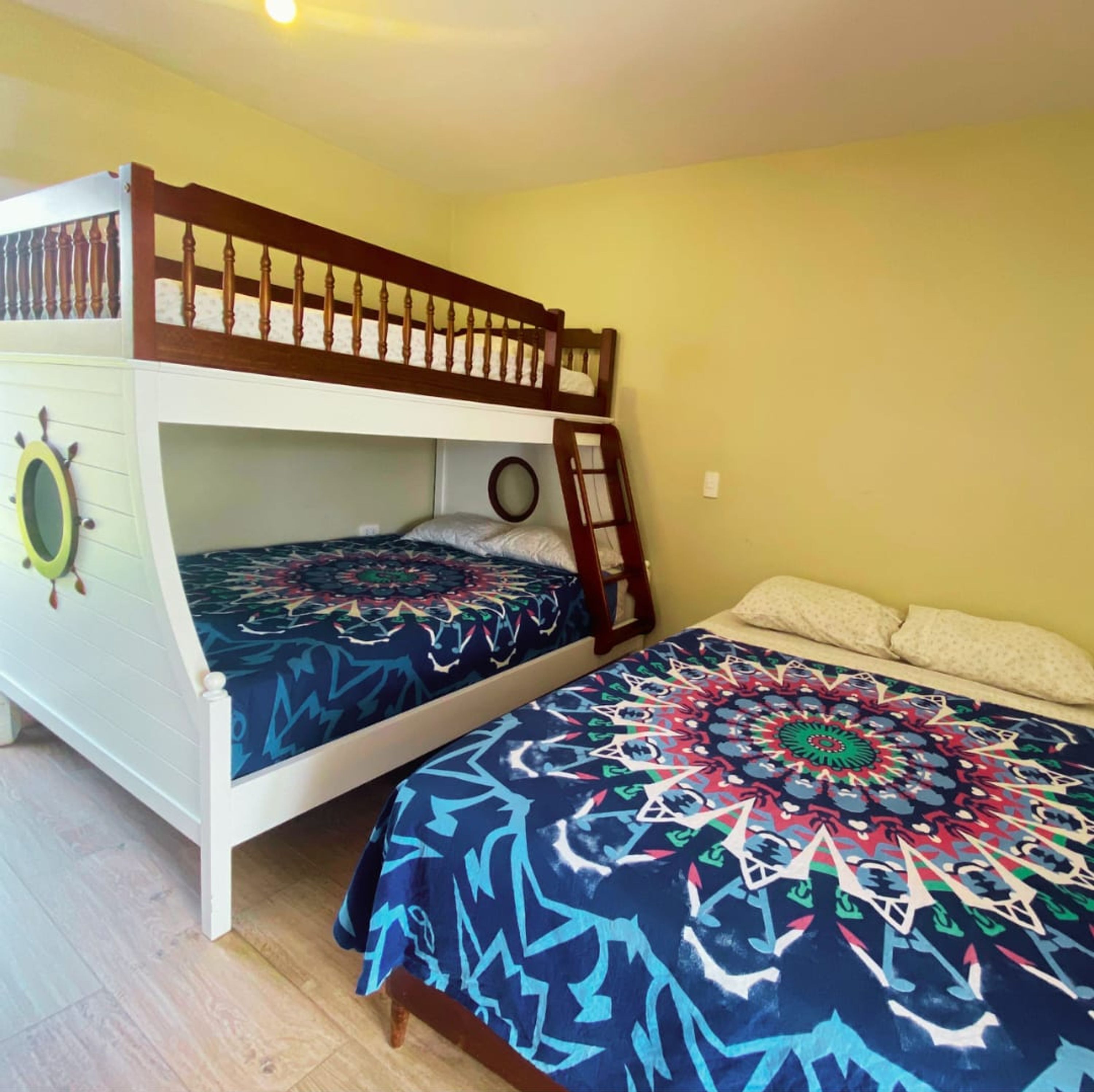 A bunk bed room with a ladder, a circular mirror, and a patterned bedspread.