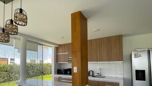 A modern kitchen with wooden cabinets, a stainless steel refrigerator, and a large island. - HOP Odaiba Exclusiva Laguna y Playa en Chincha (El Carmen)
