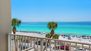 A balcony with a view of a beach with palm trees and a clear blue sky.