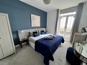 Une chambre à coucher avec un lit, une table de chevet, une lampe, une fenêtre avec des rideaux et une vue sur l’extérieur.
