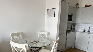 Moderni keittiö, jossa on valkoiset kaapit, lasinen ruokapöytä ja valkoiset tuolit.