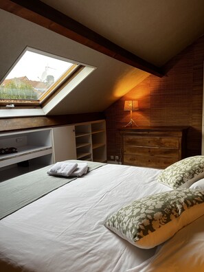 A bedroom with a skylight, a bed with floral pillows, a wooden headboard, and a bedside table with a lamp.