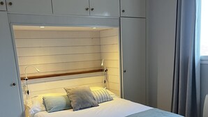 Un llit ben fet amb llençols i almoades grises, un panell de capçal de fusta i un armari gris a la part superior.
