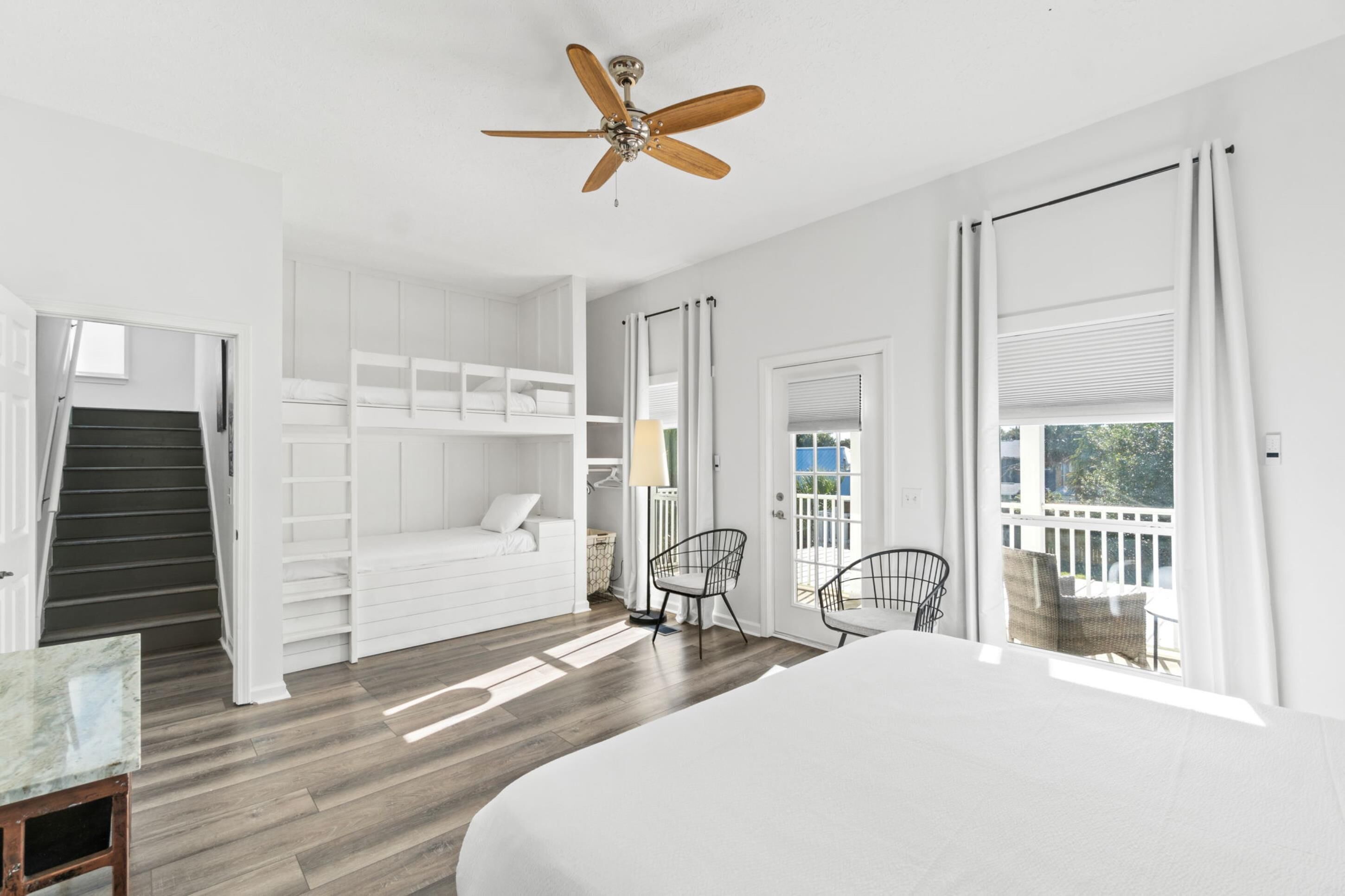 A bedroom with a bed, a ceiling fan, a staircase, a closet, and a view of the outdoors.