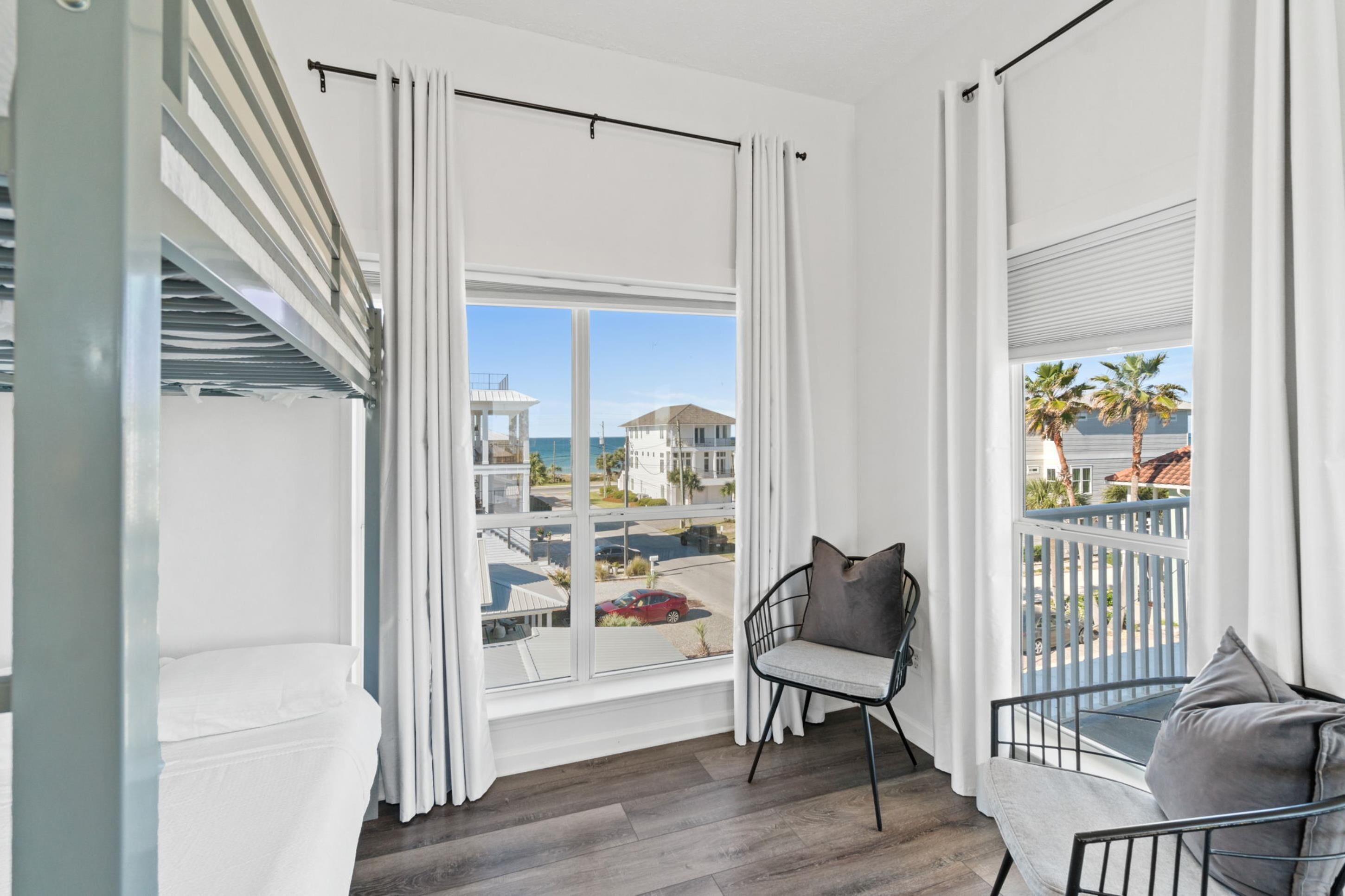 Un balcon avec vue sur l’océan et les bâtiments, une chaise avec un coussin et une balustrade.