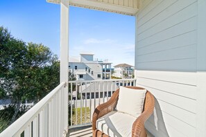A balcony with a wicker chair and a white railing, overlooking a residential area with multiple houses. - Beach House - The Sandcastle by PHG (Panama City Beach)