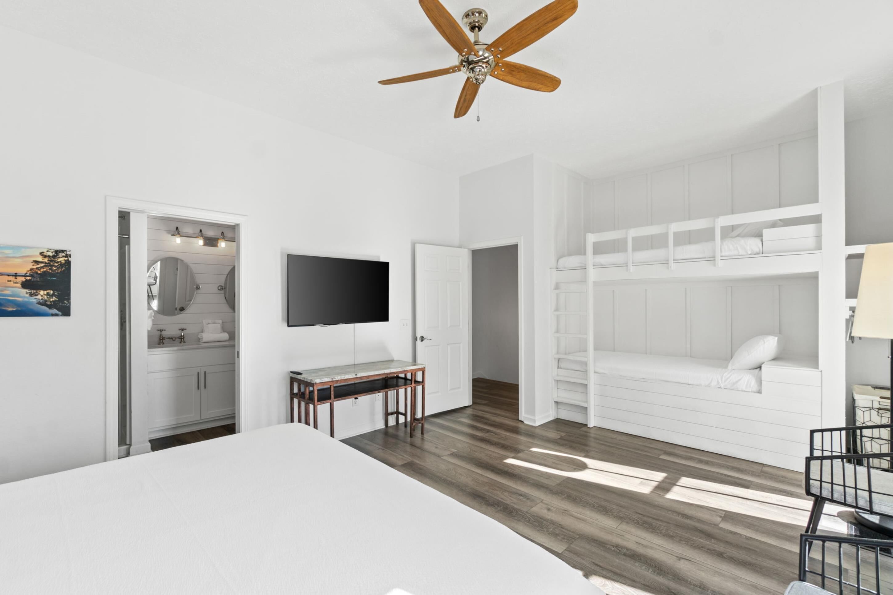A bedroom with a bed, a desk, a TV, a ceiling fan, and a bunk bed.
