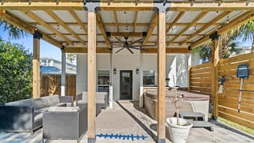 An outdoor patio area with wooden pergola, seating, and a ceiling fan.