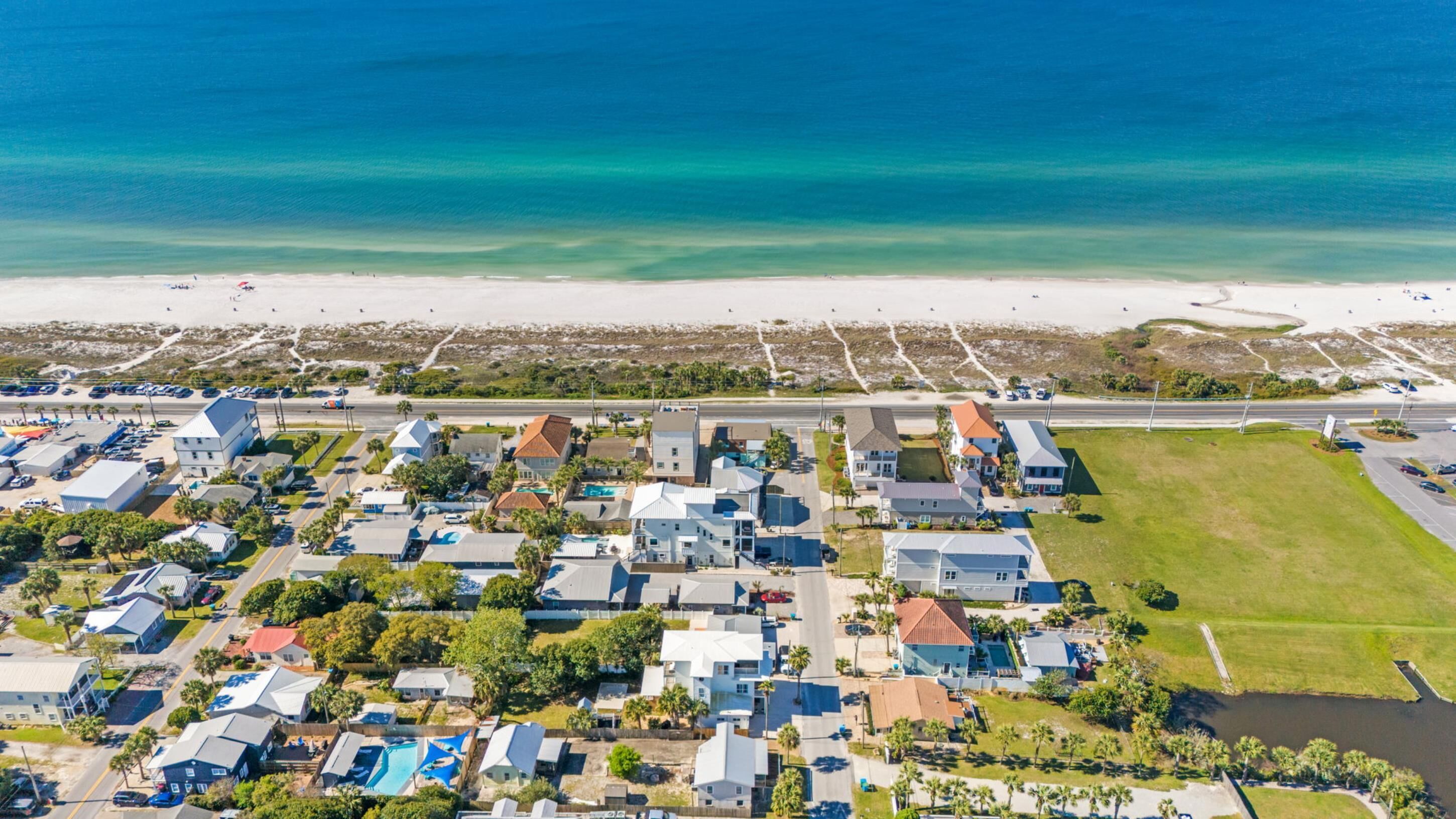 An aerial view of a coastal residential area with houses, a beach, and a road.
