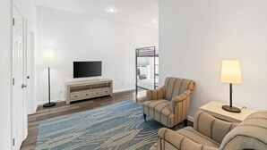 A modern living room with a flat-screen TV, a sofa, a chair, a lamp, and a wooden ceiling fan. - Beach House - The Sandcastle by PHG (Panama City Beach)