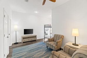 Una sala de estar moderna con un televisor de pantalla plana, un sofá, una silla, una lámpara y un ventilador de techo de madera.