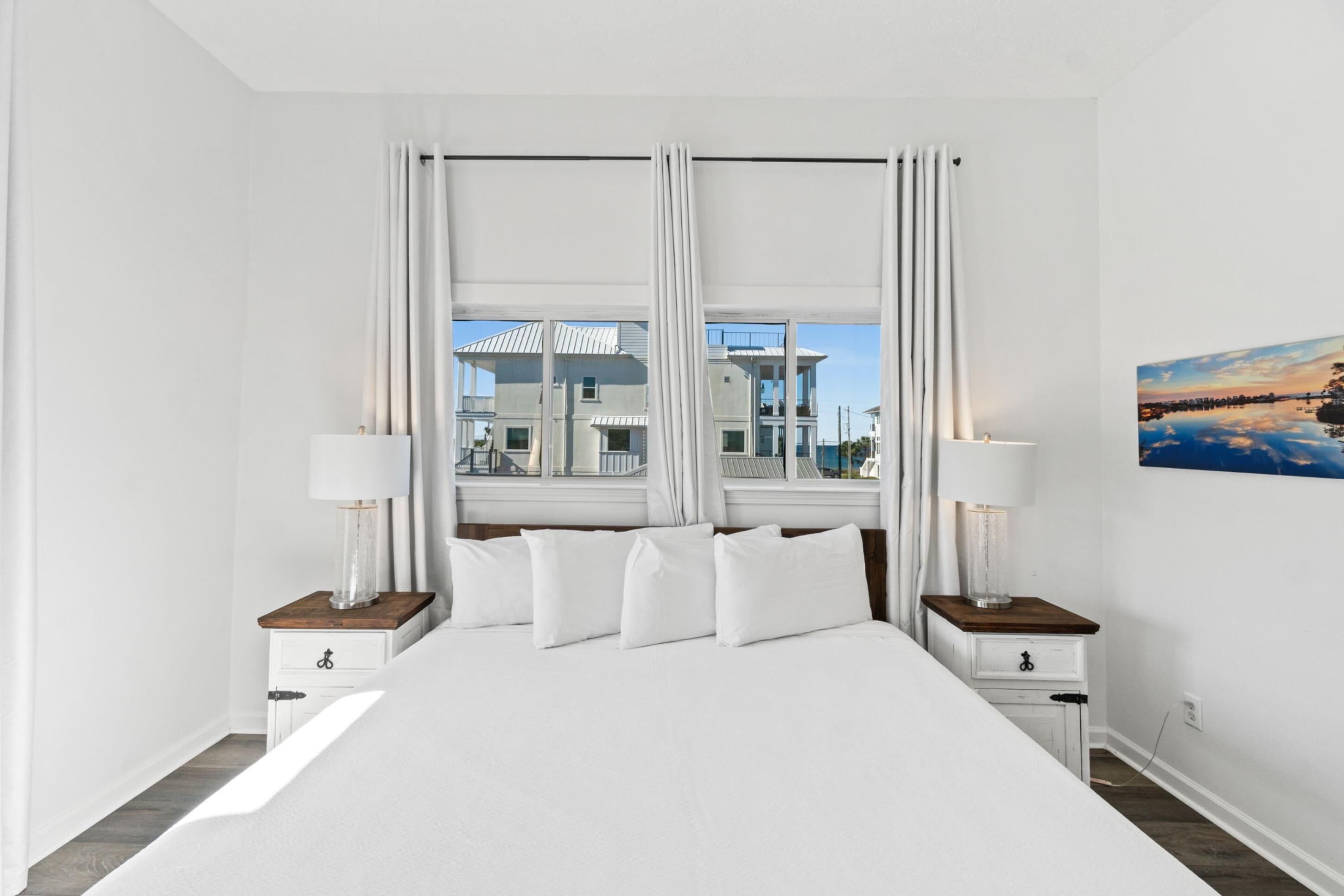 A hotel room with a large bed, two bedside tables with lamps, a view of a building through the window, and a painting on the wall.