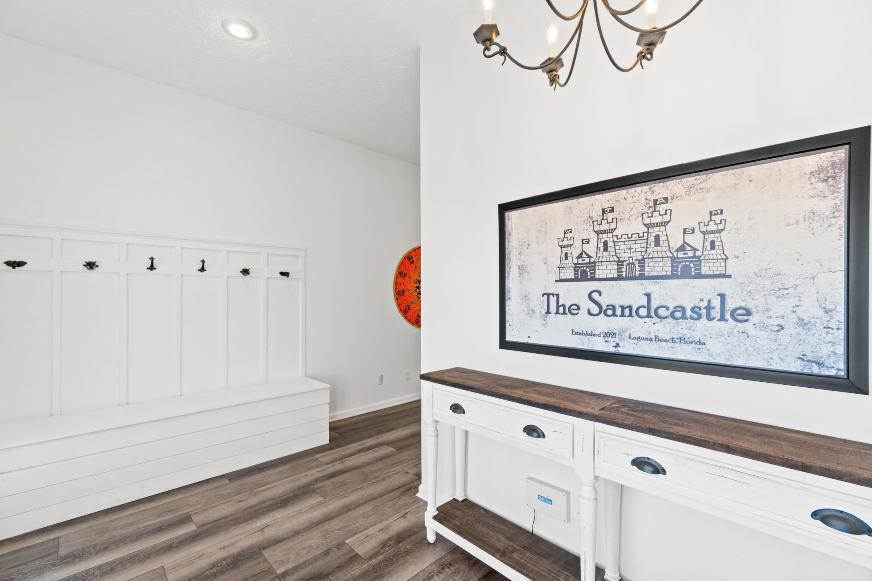 Una habitación con un banco blanco, un mueble de madera con cajones y un cuadro colgado en la pared de 'The Sandcastle', que muestra una ilustración de un castillo.