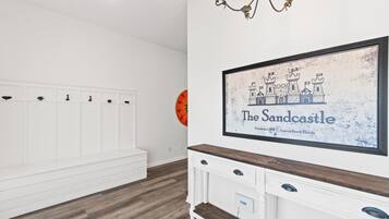 Una habitación con un banco blanco, un mueble de madera con cajones y un cuadro colgado en la pared de 'The Sandcastle', que muestra una ilustración de un castillo.