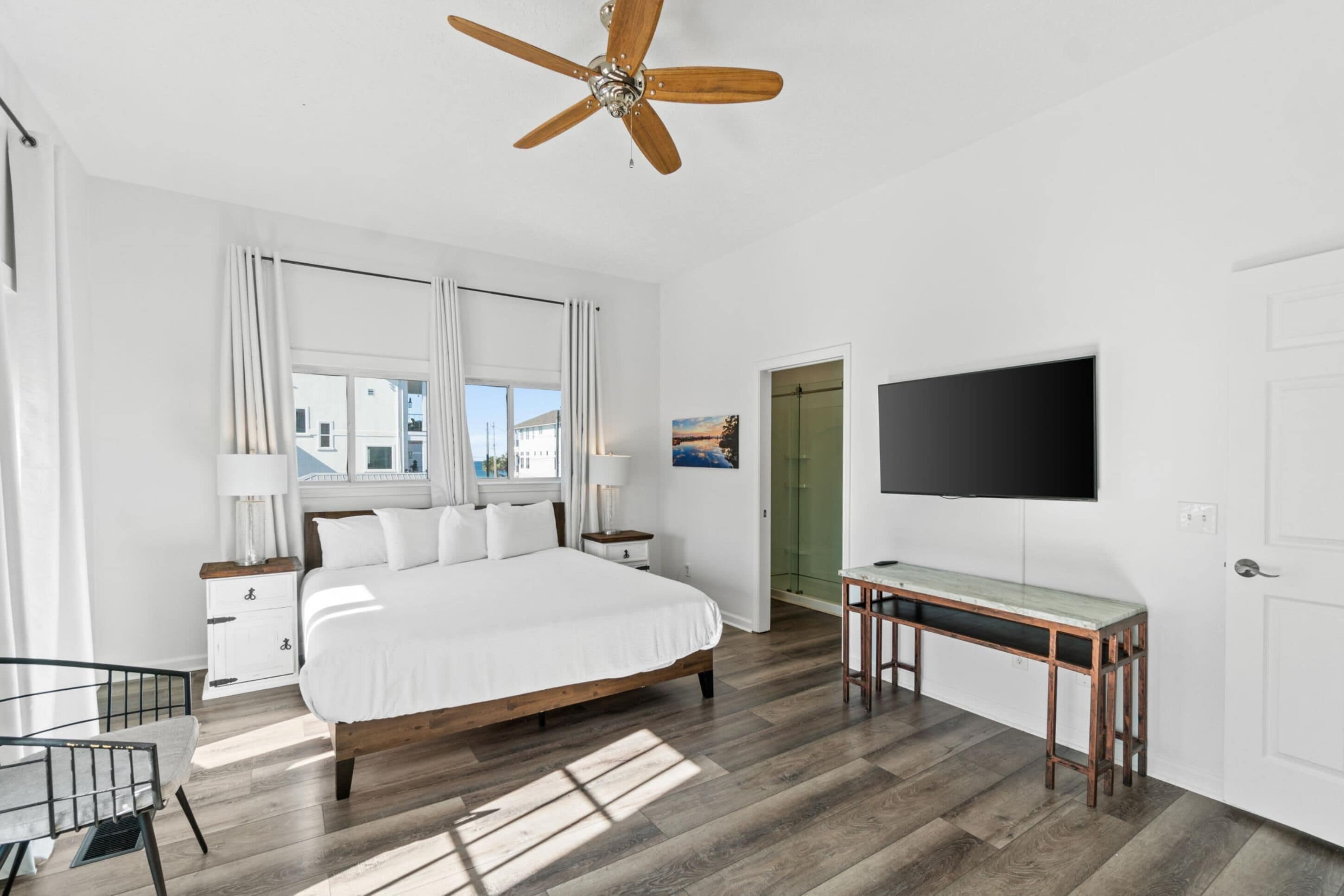 A hotel room with a bed, bedside tables, a desk, a television, and a ceiling fan.