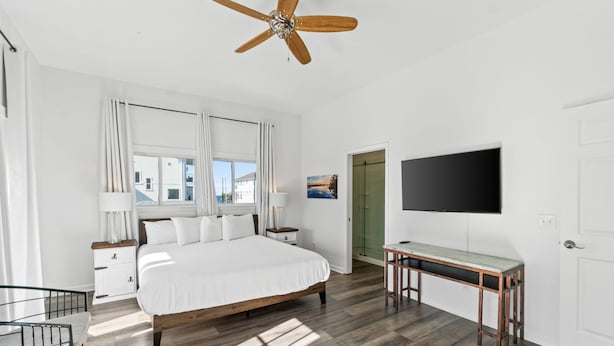 A hotel room with a bed, bedside tables, a desk, a television, and a ceiling fan. - Beach House - The Sandcastle by PHG (Panama City Beach)