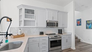 A modern kitchen with white cabinetry, stainless steel appliances, and a granite countertop. - Beach House - The Sandcastle by PHG (Panama City Beach)
