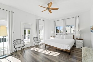 A bedroom with a large bed, two chairs, a ceiling fan, and a window with curtains. - Beach House - The Sandcastle by PHG (Panama City Beach)
