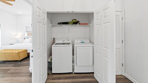 A laundry room with two white washing machines and a shelf above them. - Beach House - The Sandcastle by PHG (Panama City Beach)