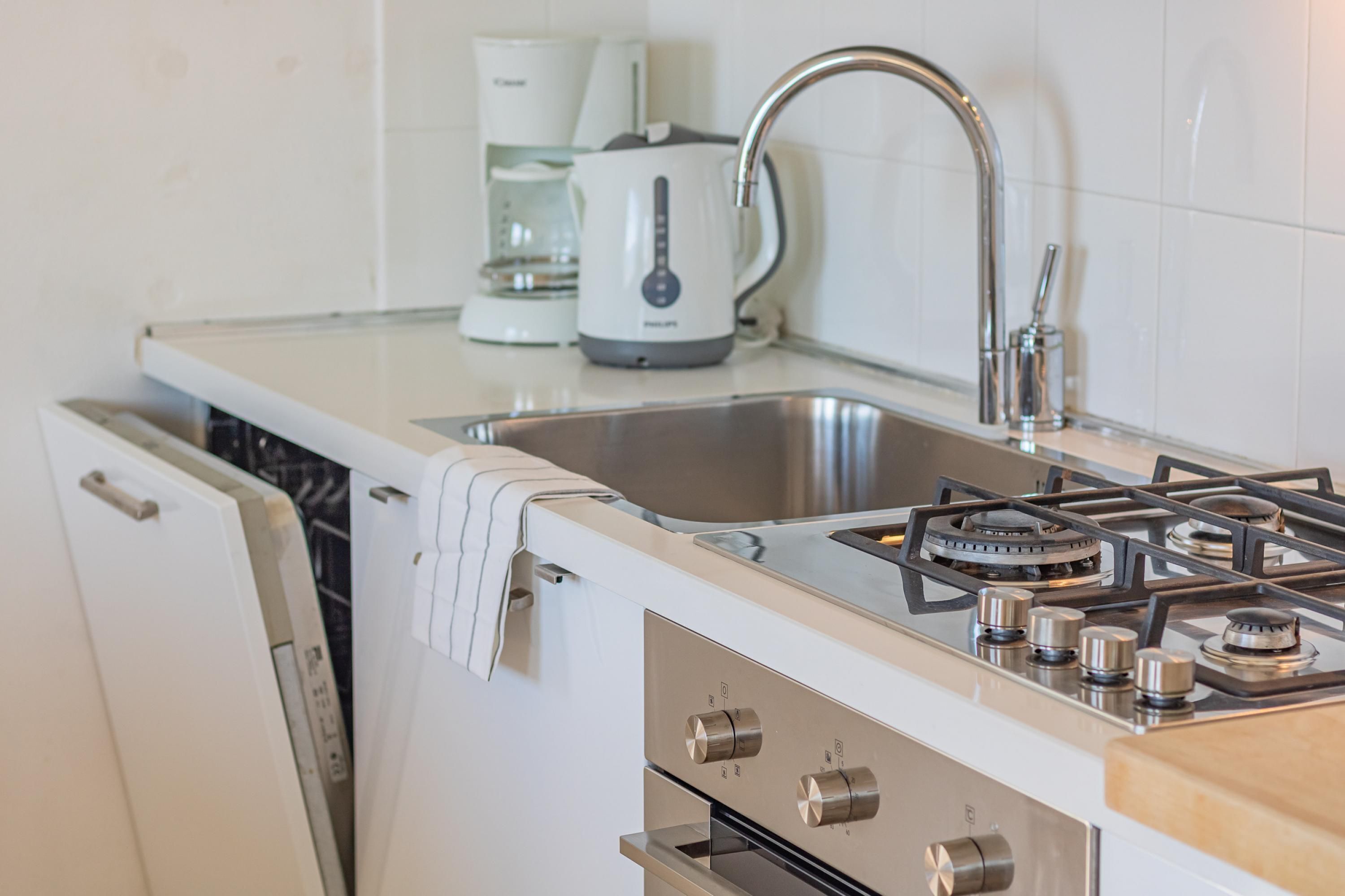 A modern kitchen with a stainless steel sink, a gas stove, and a coffee maker.
