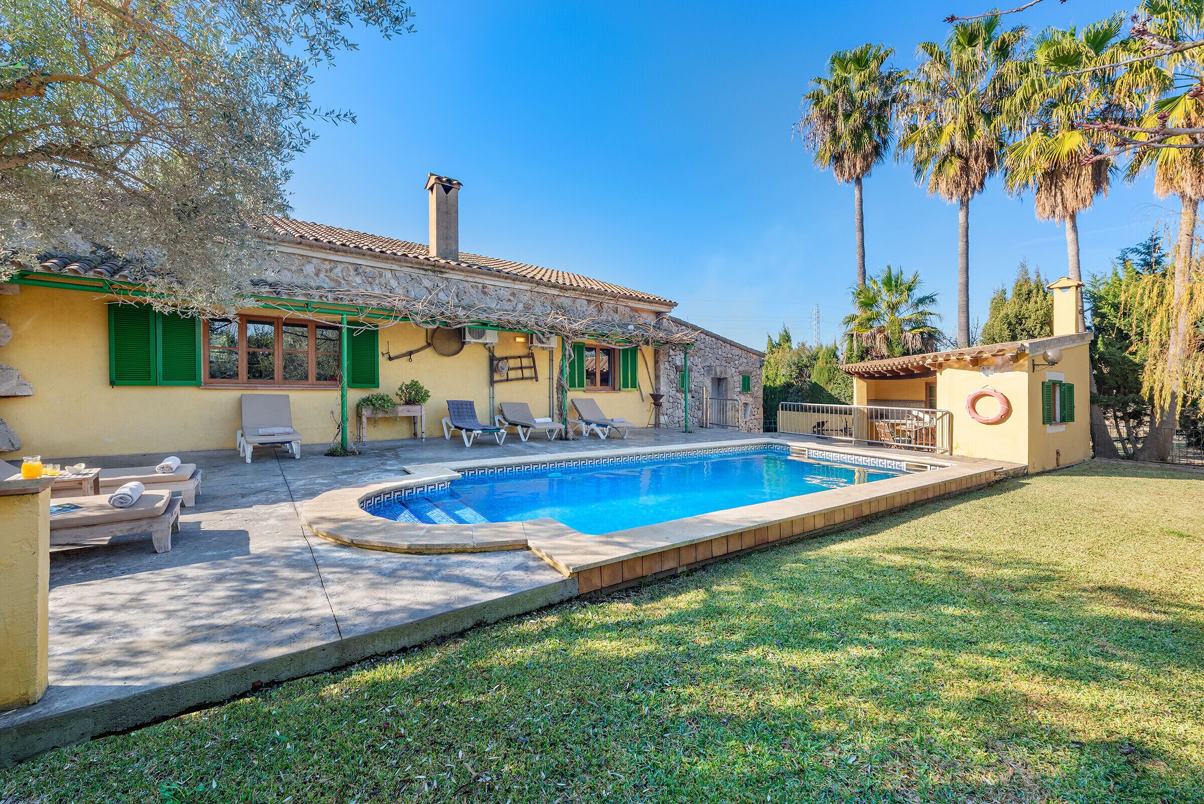 Una casa con piscina, contraventanas verdes y un patio con sillones de descanso.