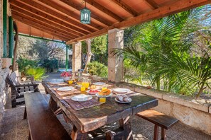 An outdoor dining area with a wooden table set for a meal, surrounded by stone walls and lush greenery. - Villa Moli Fora Terme by JS Villas (Pollensa / Pollença)