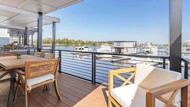 Een terras met zitplaatsen buiten, uitzicht op de jachthaven en een gebouw op de achtergrond.