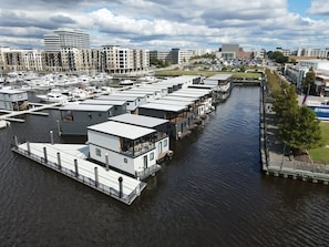 Uma marina com casas flutuantes, um cais e um horizonte urbano ao fundo.