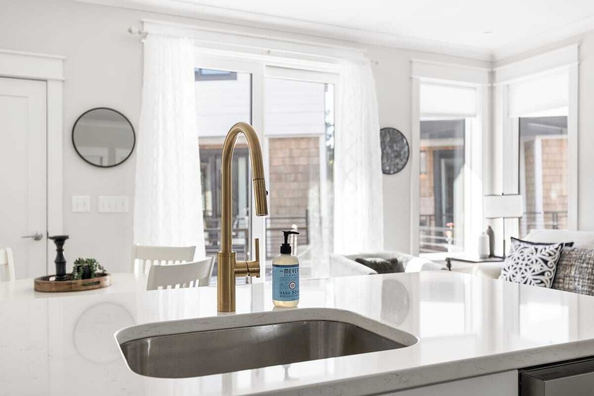 A modern kitchen with a white countertop, a gold faucet, and a bottle of hand soap.