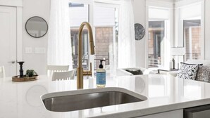 Een moderne keuken met een wit aanrecht, een gouden kraan en een fles handzeep.
