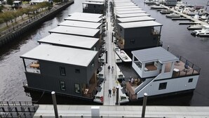 Een afgemeerd woonschip met een overdekt terras, een klein zitgedeelte buiten en een pad naar de steiger.