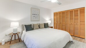 Un dormitorio con cama, lámparas de noche, ventilador de techo, armario de madera y un interruptor de luz en la pared.