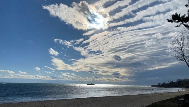 Une plage avec un ciel dégagé, un rivage sablonneux et une vue lointaine sur un promontoire rocheux.