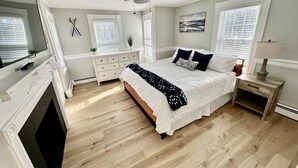 Une chambre à coucher comprenant un lit, un ventilateur de plafond, une télévision, une cheminée, une commode et une fenêtre avec des stores.