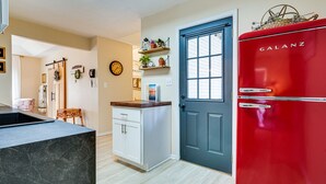 A kitchen with a black marble countertop, white cabinets, a red Galanz refrigerator, and a blue door.