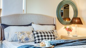 A neatly made bed with a checkered pillow, a cup of coffee, and a donut on a tray.