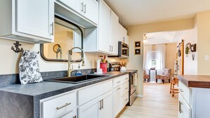 A modern kitchen with white cabinets, a black countertop, and a large mirror. There is a sink, stove, and a dining area in the background.