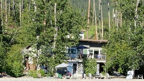Una propiedad junto al lago con una casa de dos pisos, asientos al aire libre y un muelle.