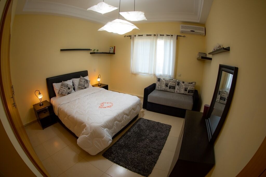 Een slaapkamer met een bed, nachtkastjes, een dressoir, een spiegel en een raam met gordijnen.