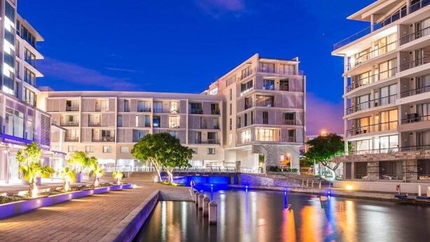 A modern hotel with multiple floors, a central courtyard with a water feature, and outdoor lighting. - Contemporary Cape Town Gem- No Loadshedding (Cape Town)