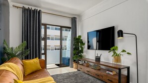 A modern living room with a leather sofa, a grey rug, a wooden console table with a TV, and a large plant. - Chic Beachfront Oasis - Balcony - Netflix (Cape Town)