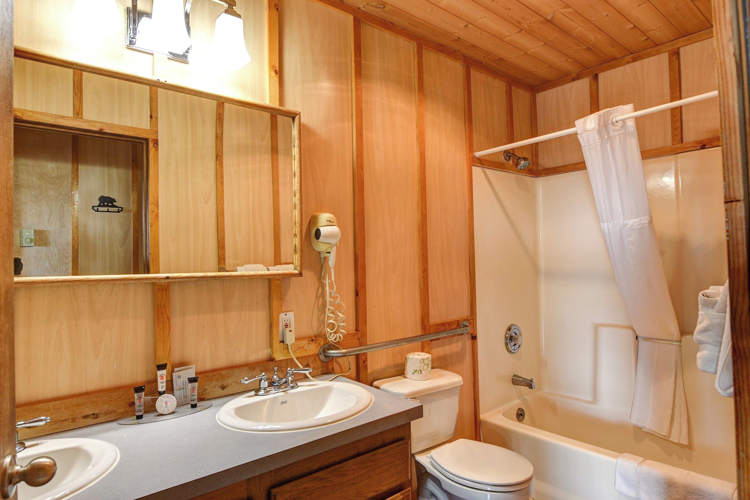A wooden-paneled bathroom with two sinks, a toilet, and a bathtub.