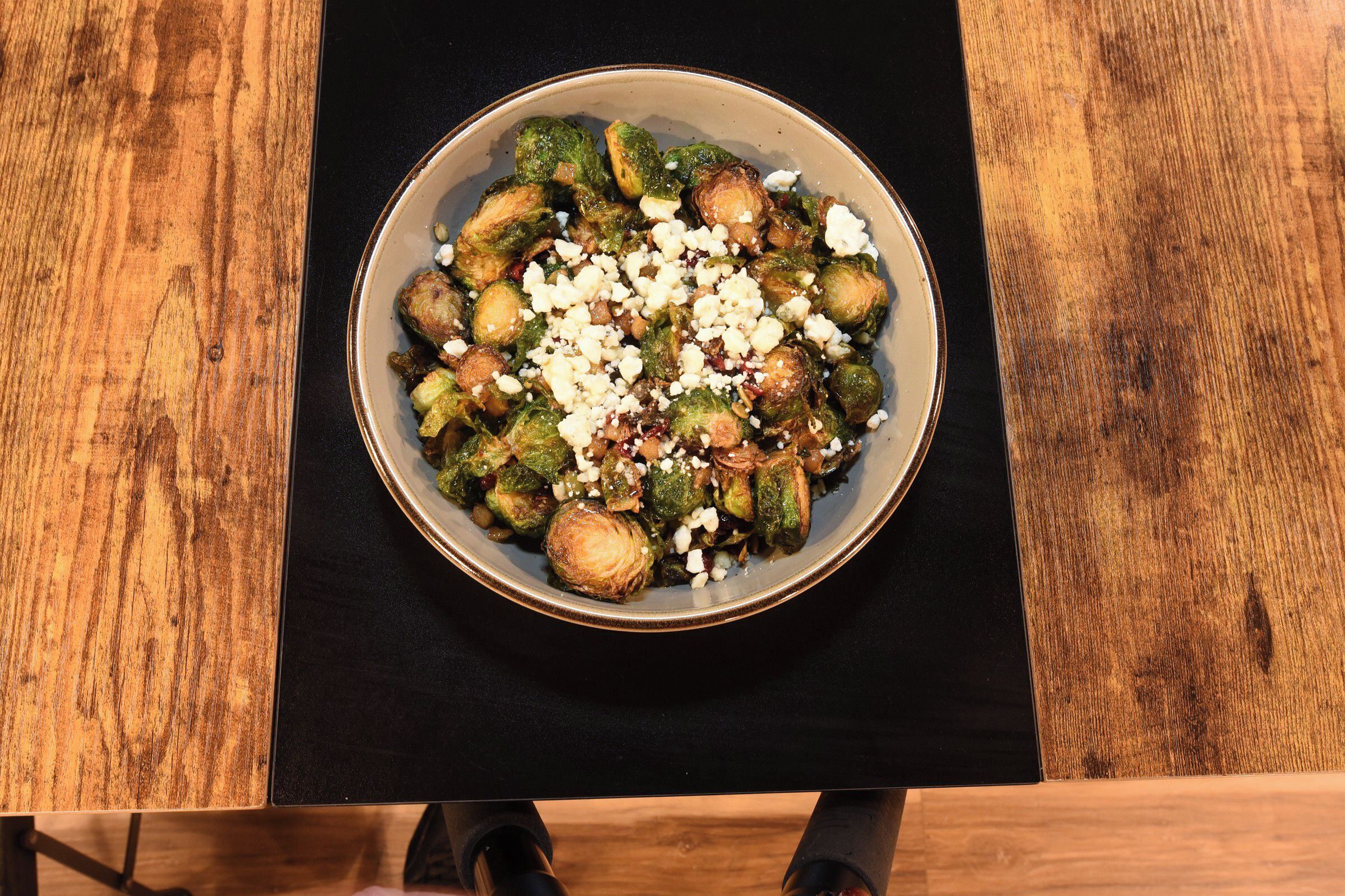 A bowl of Brussels sprouts topped with cheese on a wooden table.