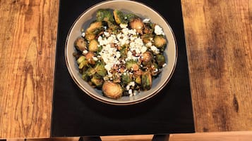 A bowl of Brussels sprouts topped with cheese on a wooden table.
