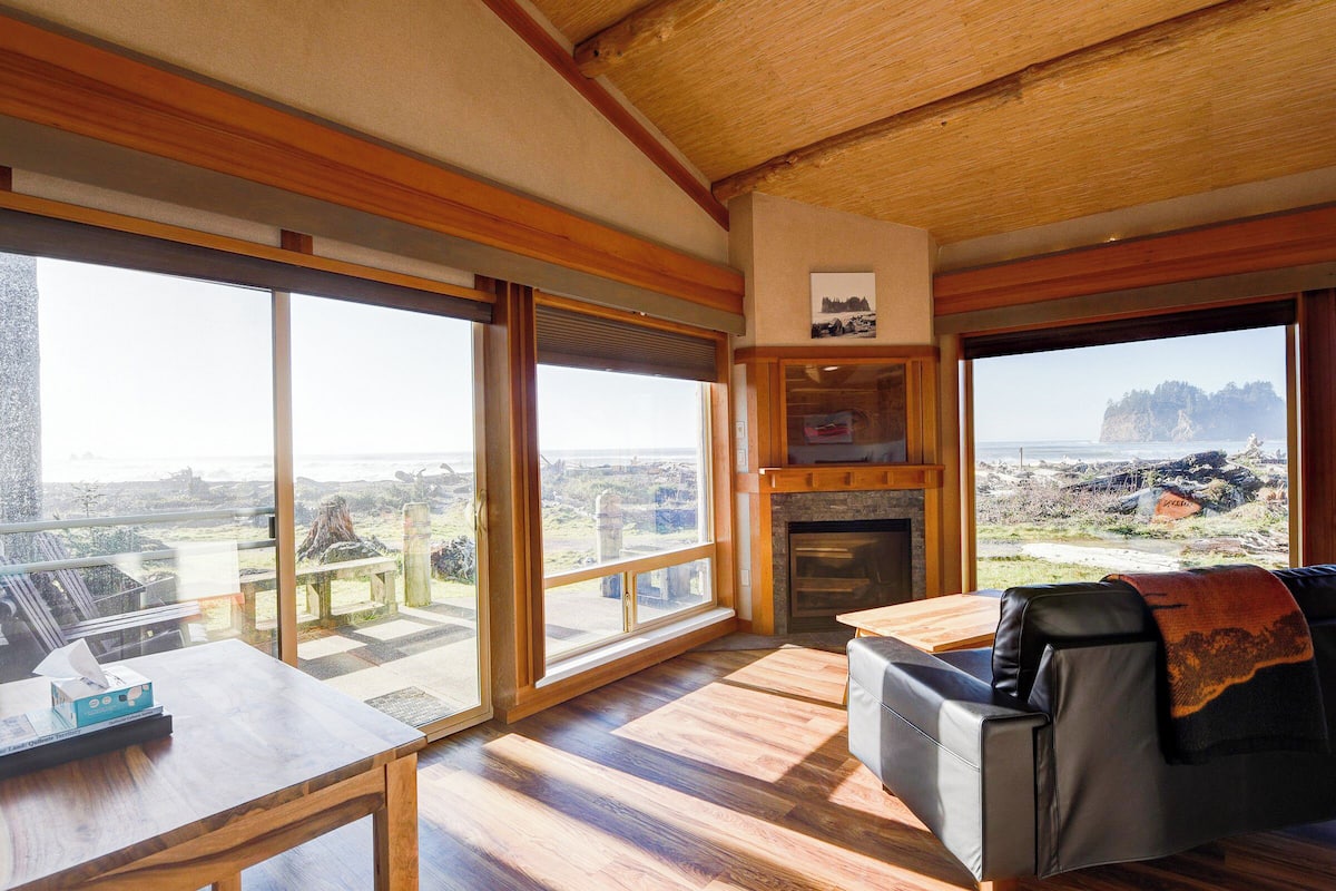 A spacious living room with large windows, a fireplace, and a view of the landscape.