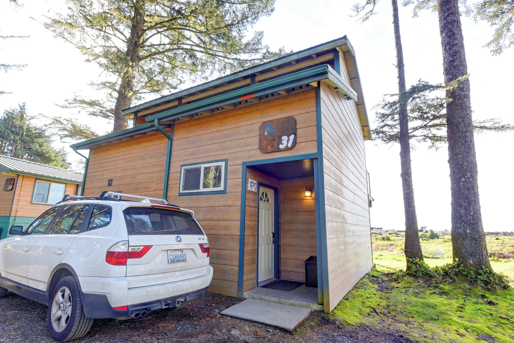 A small wooden cabin with a number 31 sign, a car parked in front, and a door leading to the entrance.