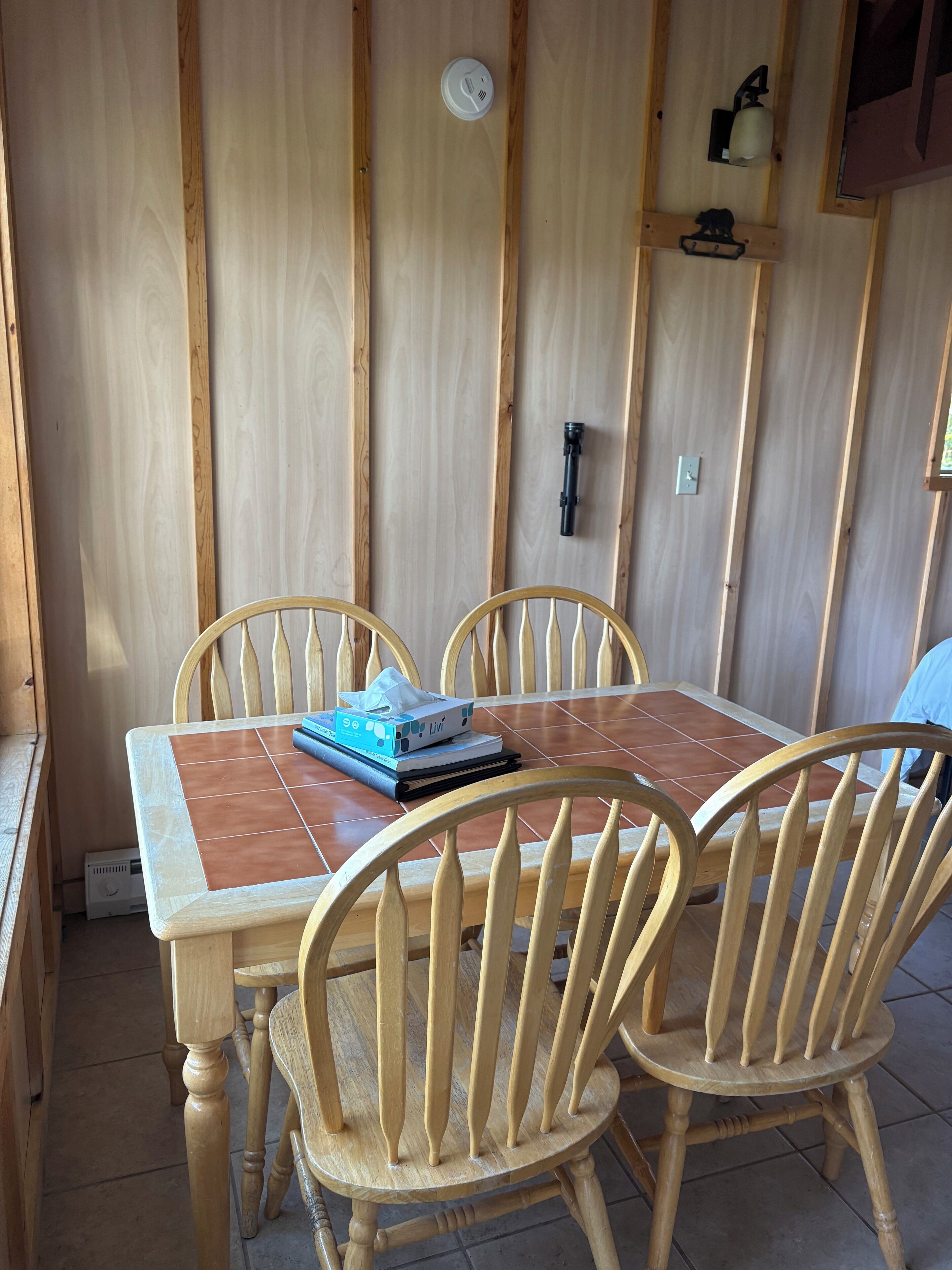 A wooden dining table with four chairs, a tissue box, and a small electronic device on the table.