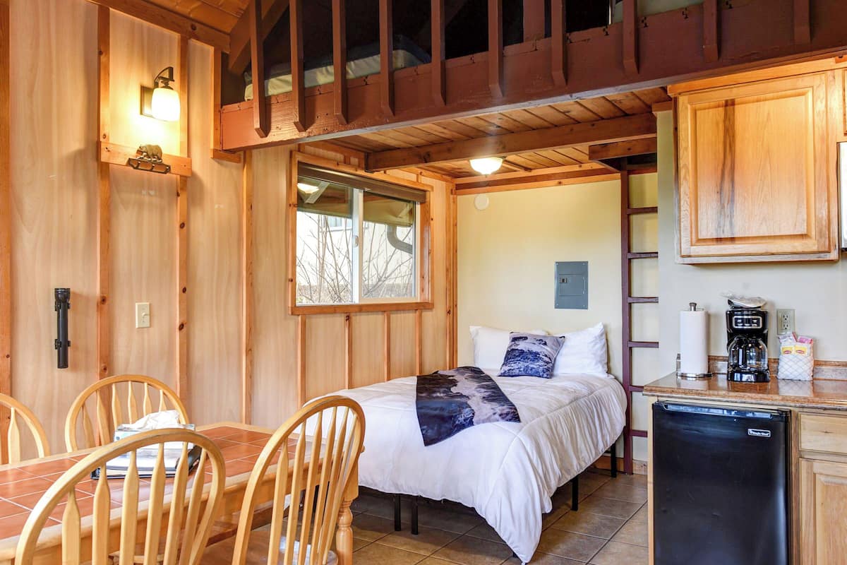A compact room with a bed, a dining table with chairs, a small kitchenette, and a window.